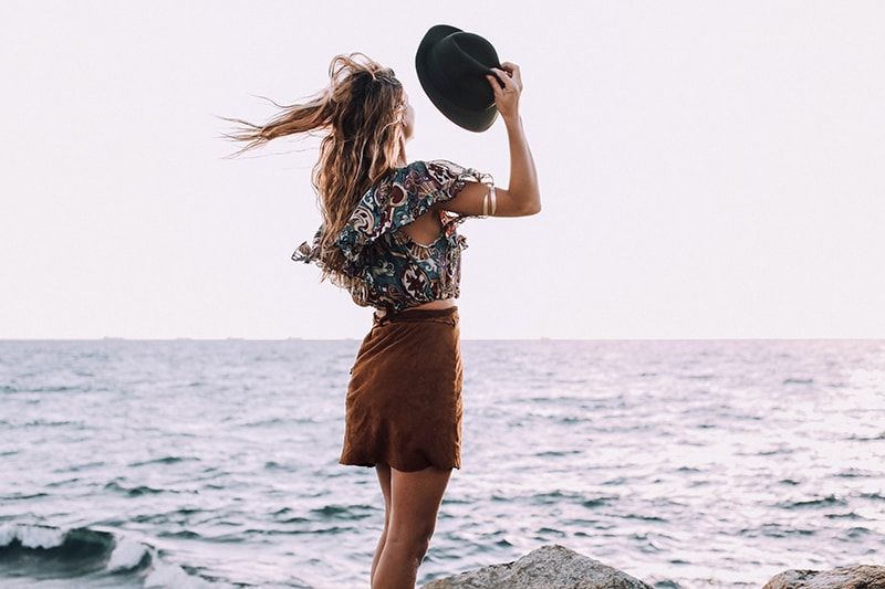 Frau mit Hut steht im Wind am Meer