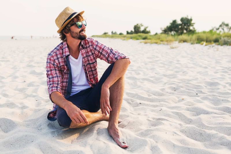 Ein lächelnder Mann mit Hut auf dem Kopf sitzt am Strand