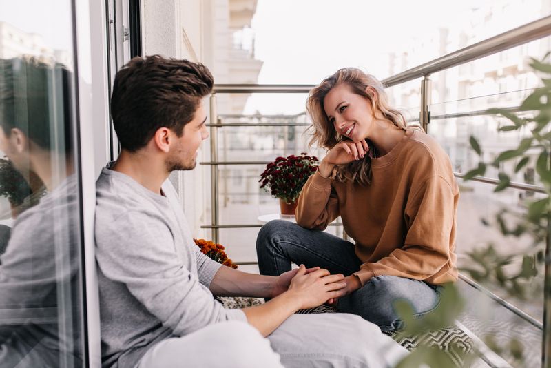 Ein lächelnder Mann und eine lächelnde Frau sitzen auf dem Balkon und unterhalten sich