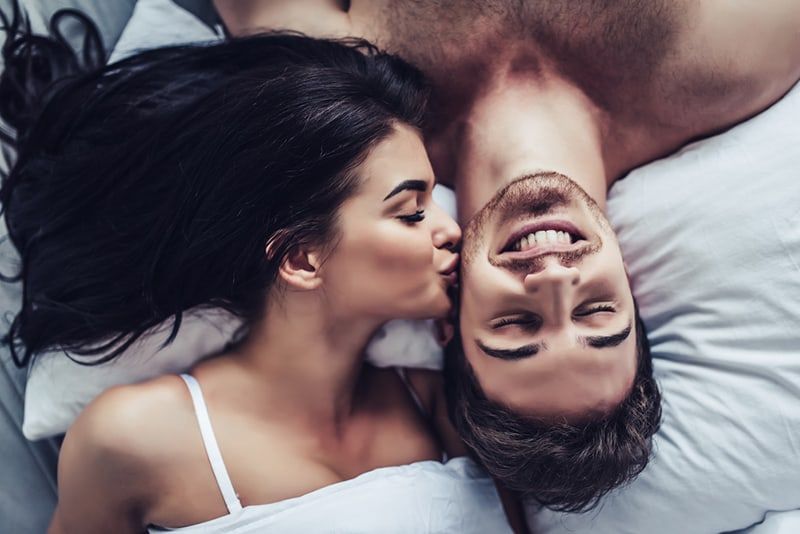 Frau küsst ihren Freund auf die Wange, während sie zusammen im Bett liegt