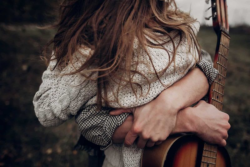 Mann umarmt eine Frau, während er eine Gitarre hält