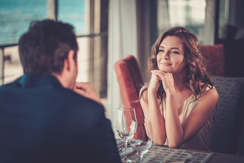 Lächelnde Frau, die aufmerksam einem Mann zuhört, der ihr gegenüber im Restaurant sitzt