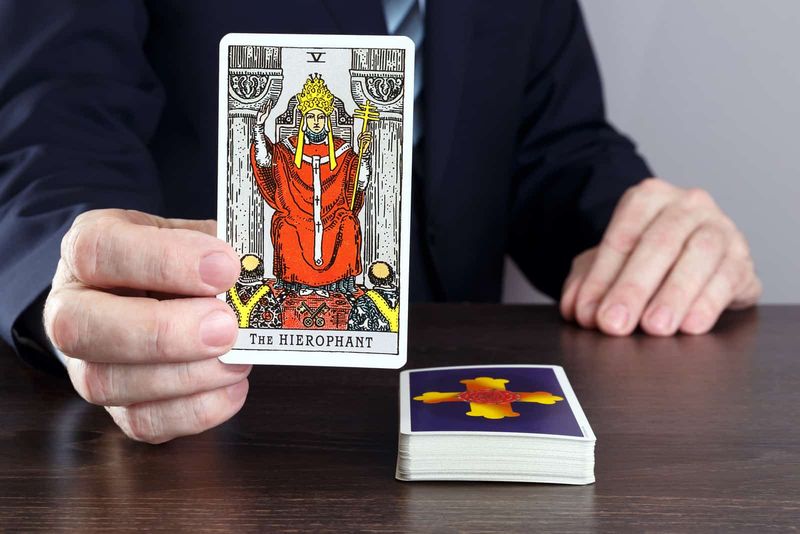 Mann hält die Hierophant-Tarotkarte über dem Tisch