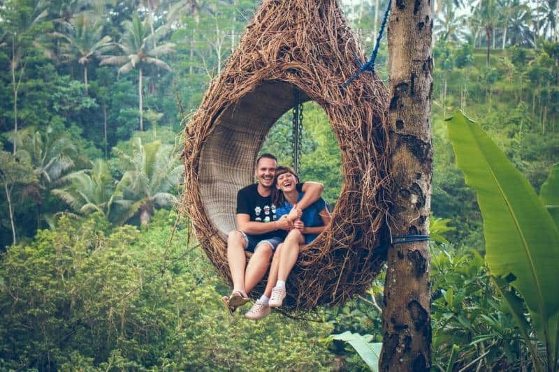 Glückliches Mann- und Frauenpaar, das auf einem Hängesessel an einem Baum sitzt
