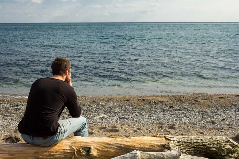 Ein Mann sitzt am Strand und blickt nachdenklich auf das Meer