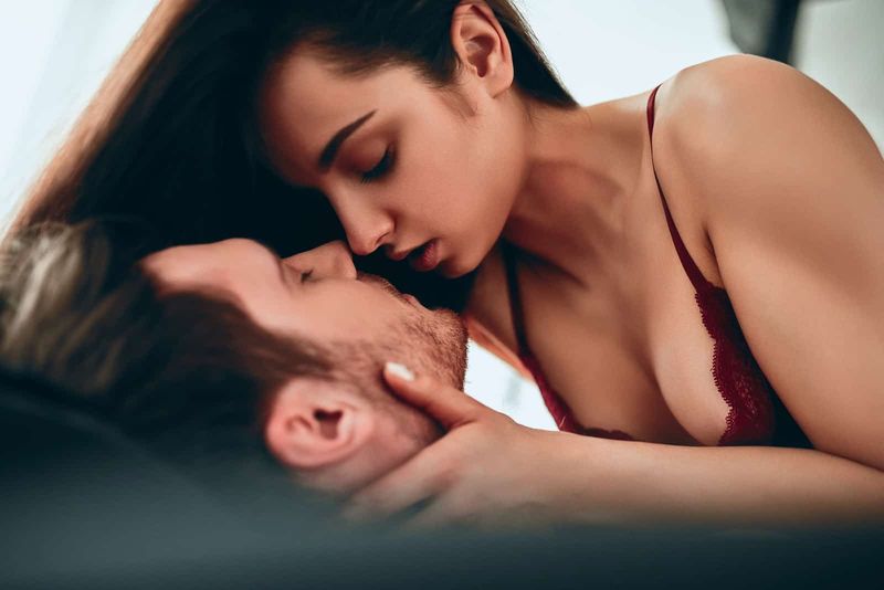 Eine braunhaarige Frau küsst einen Mann im Bett