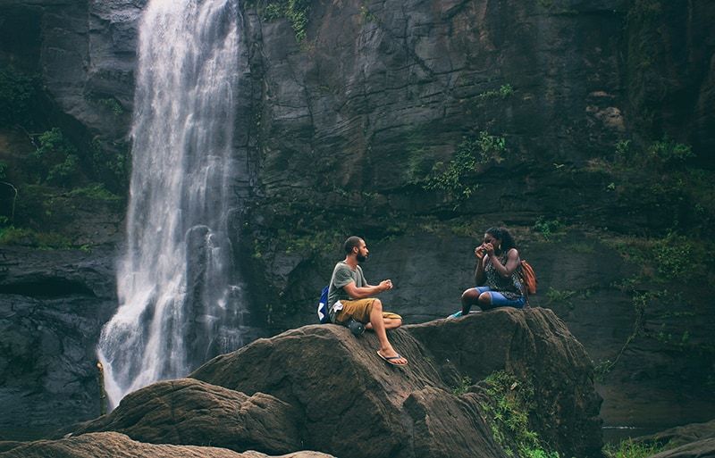 Mann und Frau sitzen auf dem Felsen in der Nähe des Wasserfalls