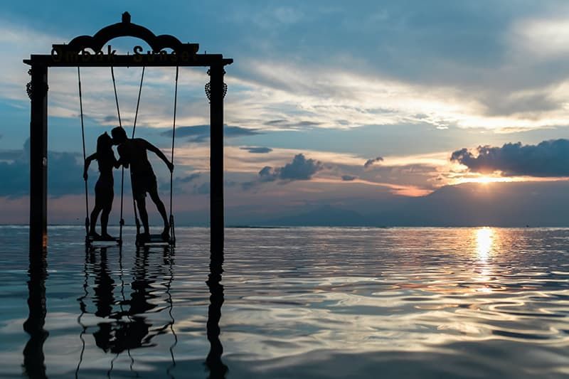 Silhouette eines küssenden Paares, das auf Schaukeln unter dem Meer steht