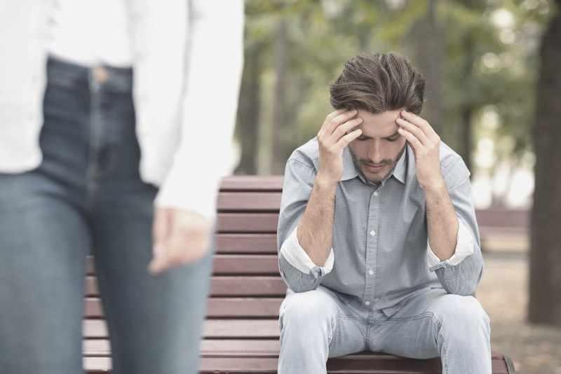 Scheidungskonzept für junges Paar. Mann sitzt auf einer Bank im Freien, während die Frau weggeht