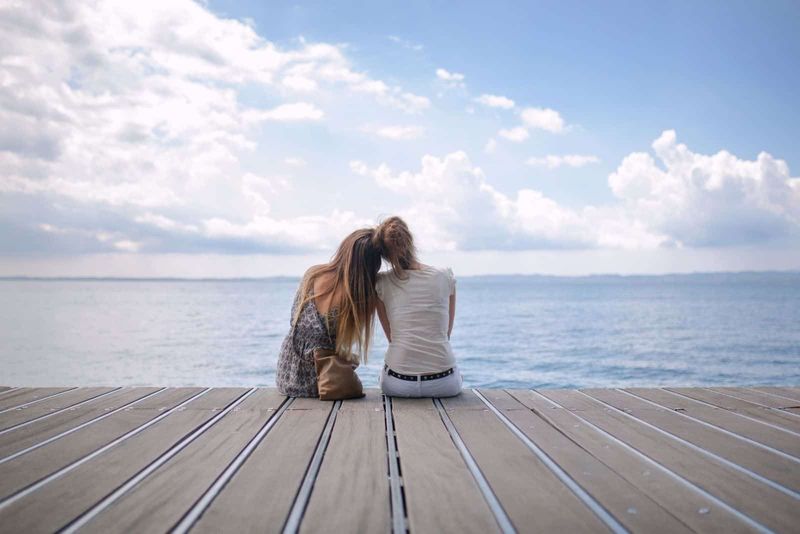 Zwei Freunde sitzen auf einem Netz vor dem Meer und lehnen sich aneinander und genießen die wunderschöne Aussicht