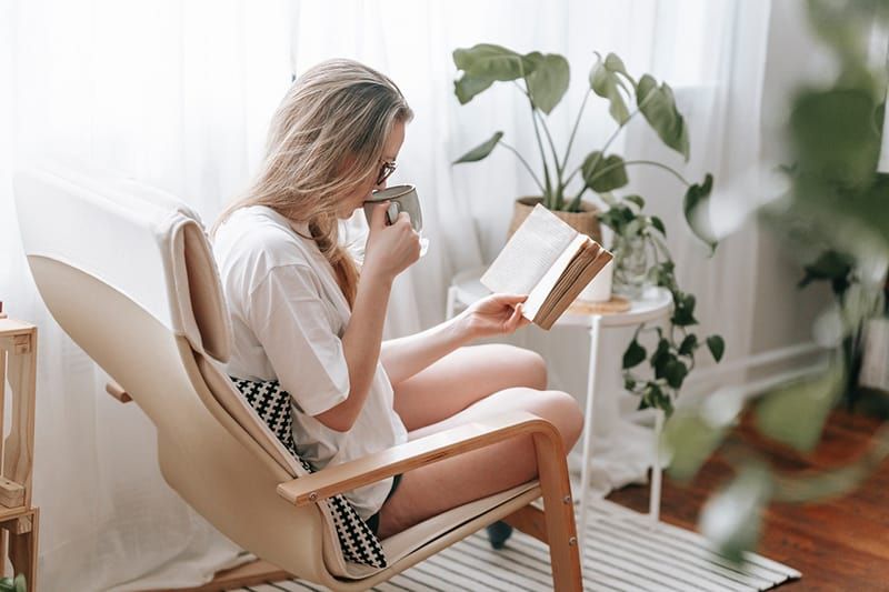 Frau liest ein Buch und trinkt Kaffee zu Hause
