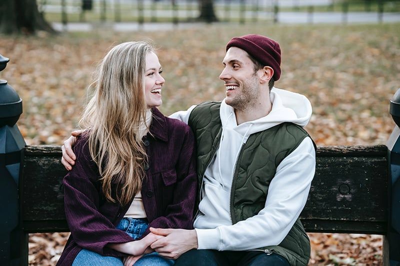 Lächelndes Paar, das auf der Bank im Park sitzt und Händchen hält