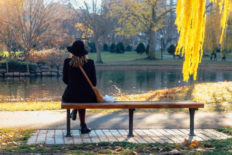 Frau mit schwarzem Hut, die auf einer Bank sitzt und auf Wasser blickt