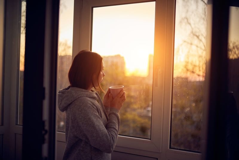 Eine Frau steht mit Kaffee in der Hand am Fenster