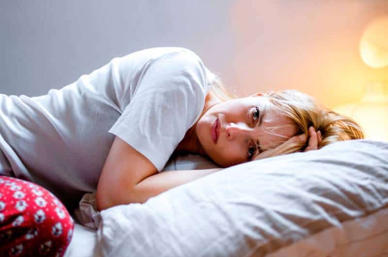 Verzweifelte Frau liegt im Schlafanzug auf dem Bett