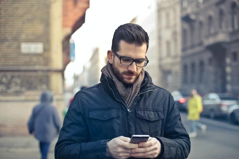 Mann mit Brille und Mantel schreibt SMS auf seinem Handy