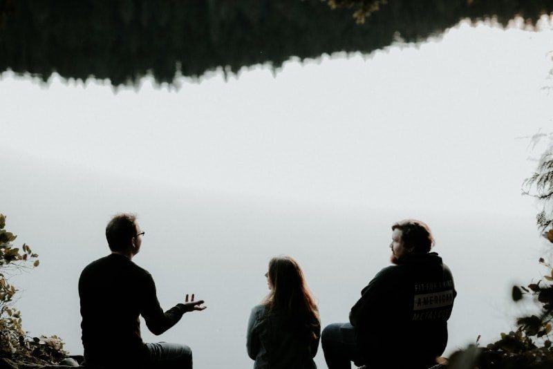 Drei Leute sitzen am Wasser und unterhalten sich