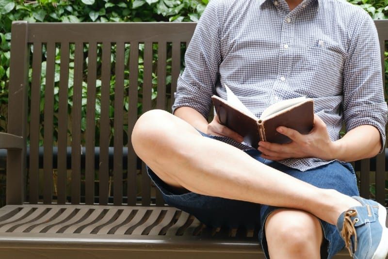 Mann liest ein Buch, während er auf einer Bank sitzt