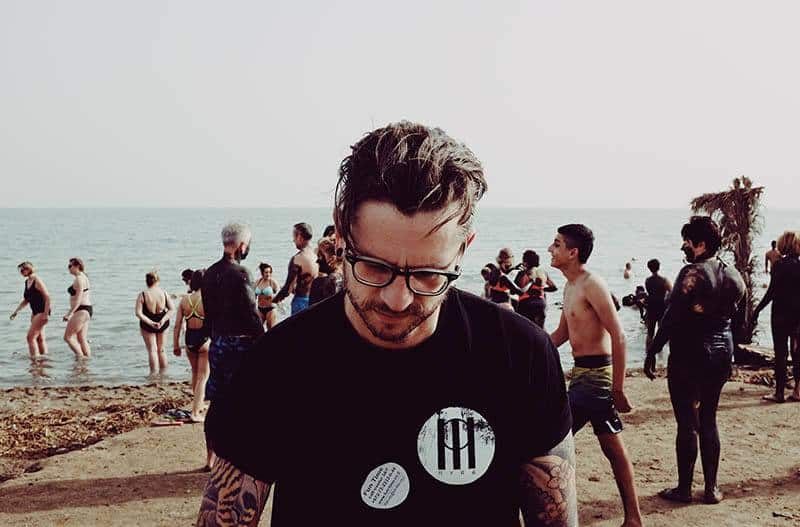 Mann mit schwarzem Hemd und Brille am Strand spazieren