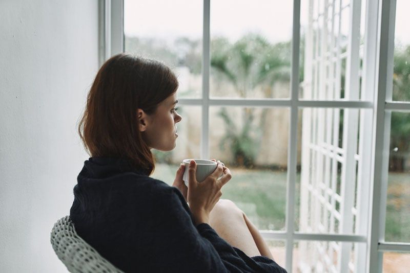 Achtsame Frau trinkt Kaffee am Fenster