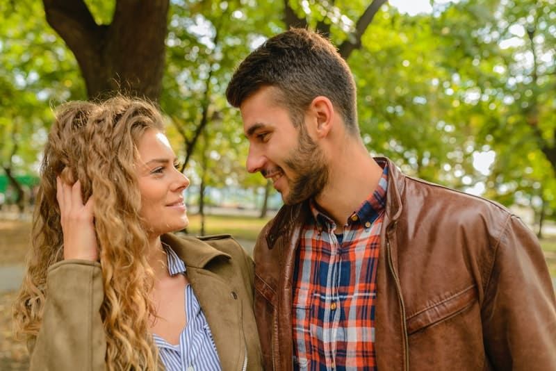 Mann und Frau sehen sich in braunen Lederjacken im Park auf Augenhöhe