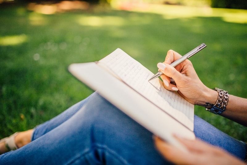 Frau schreibt auf weißem Papier, während sie auf Gras sitzt