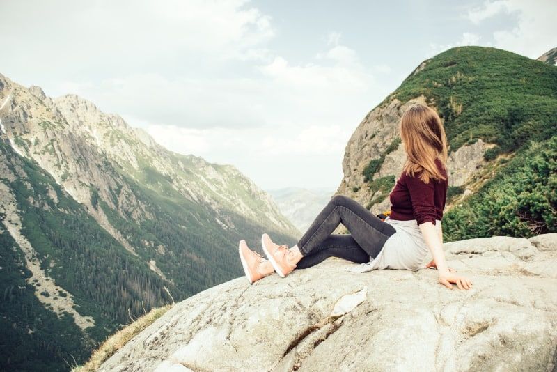 Frau, die auf einem Felsen sitzt und den Berg betrachtet