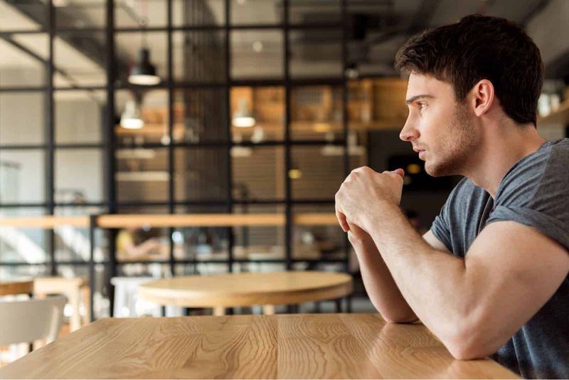 Junger Mann sitzt im Café und denkt über etwas nach