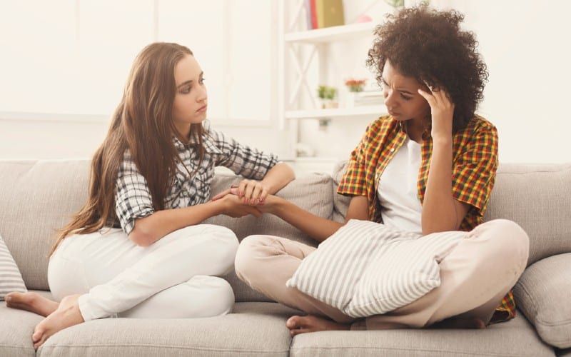 Traurige Frau spricht mit einer Freundin, während sie auf einem weißen Sofa sitzt