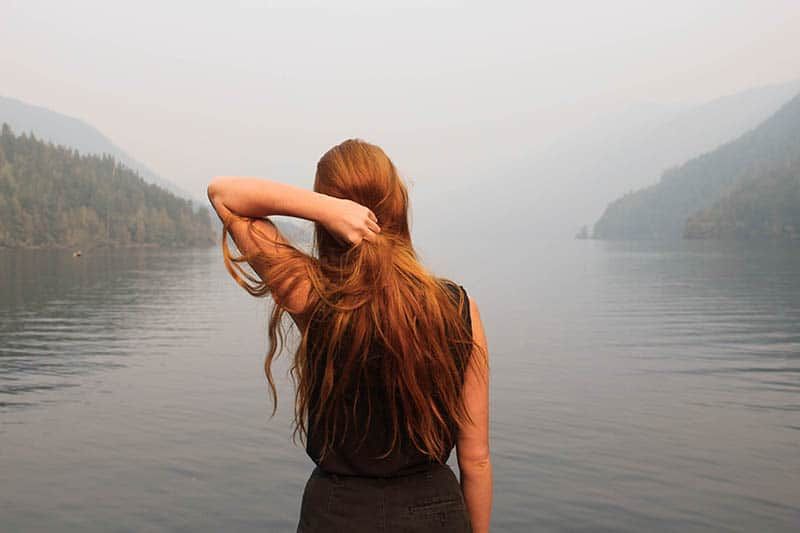 Frau mit roten Haaren, die am See steht