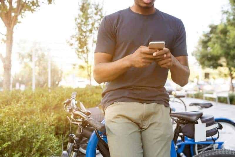 Mann, der auf seinem Telefon tippt, während er sich auf das Fahrrad lehnt