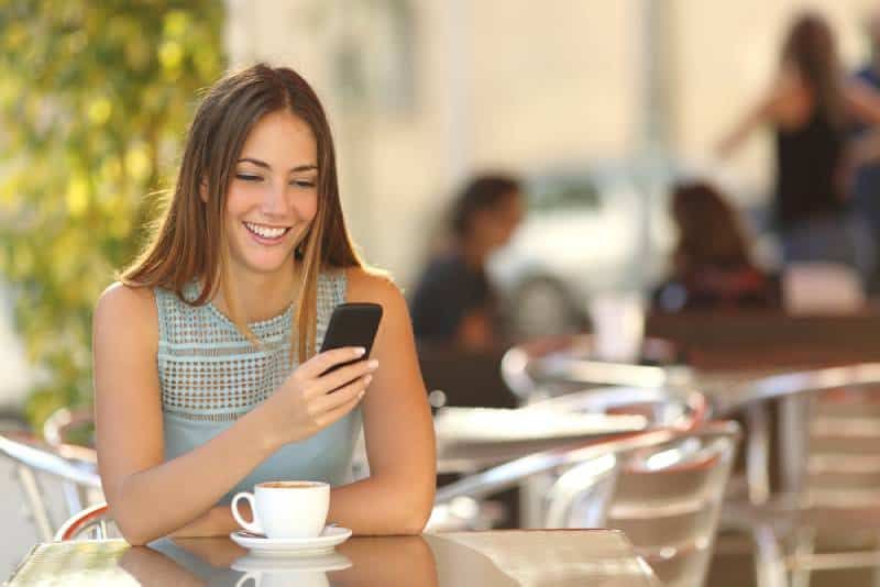 Glückliches Mädchen, das im Café auf ihr Telefon schaut