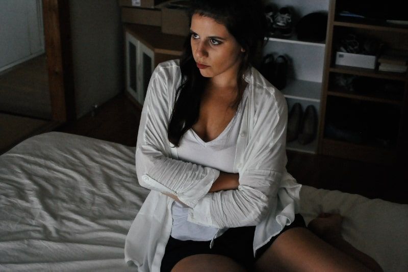 Wütende Frau in weißer Strickjacke sitzt auf dem Bett