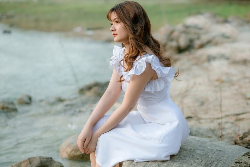 Frau im weißen Kleid sitzt auf Stein