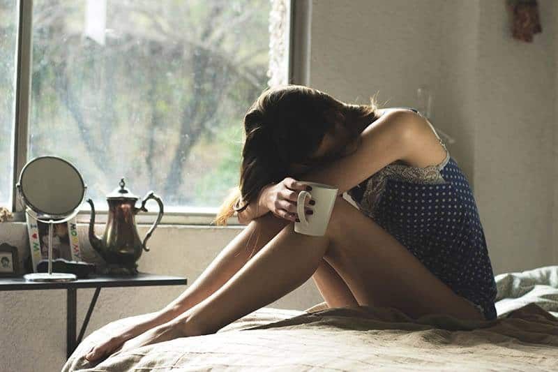 Traurige Frau sitzt auf dem Bett und hält eine Tasse