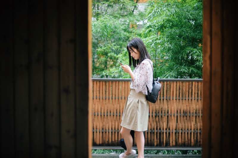 Asiatisches junges Mädchen, das beim Gehen in der Natur eine SMS auf ihrem Telefon schreibt