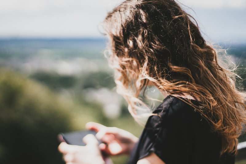 Mädchen mit langen Haaren SMS in einem unscharfen natürlichen Hintergrund