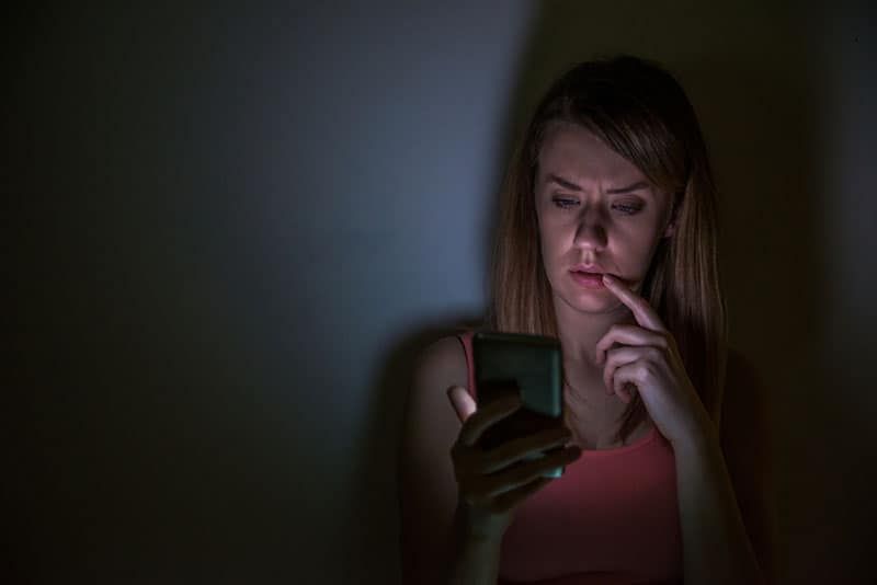 Besorgte Frau schaut nachts zu Hause auf ihr Telefon