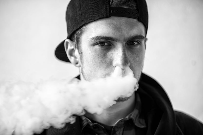 Porträt eines jungen gutaussehenden Mannes mit Mütze, der eine elektronische Zigarette raucht