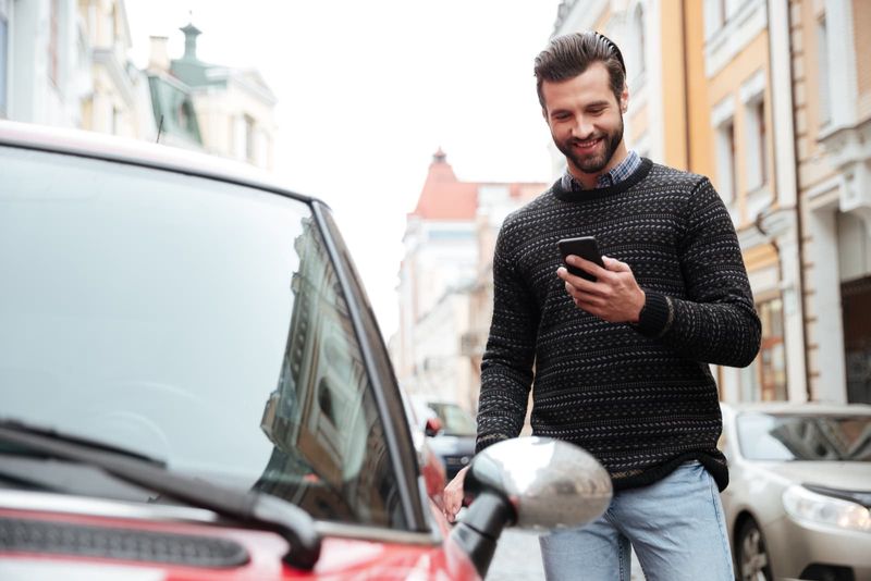 Porträt eines zufriedenen jungen Mannes im Pullover, der sein Mobiltelefon benutzt