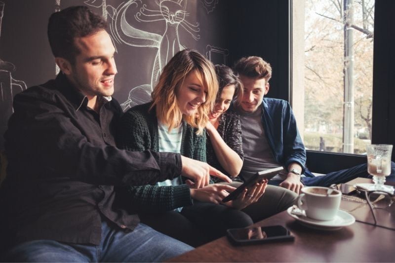 Eine Gruppe von Freunden unterhält sich im Café und schaut sich das Internet im Café an