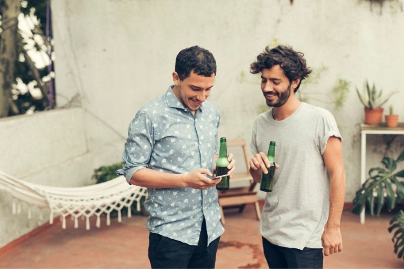 Mann teilt einem Freund die Nummer seines Telefons mit, während er draußen Bier trinkt