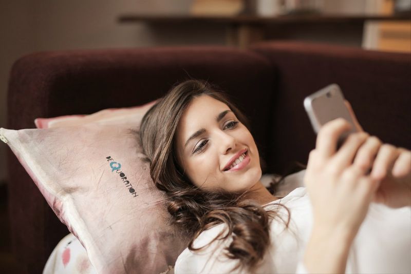 glückliche Frau, die auf der Couch liegt, während sie das Smartphone benutzt