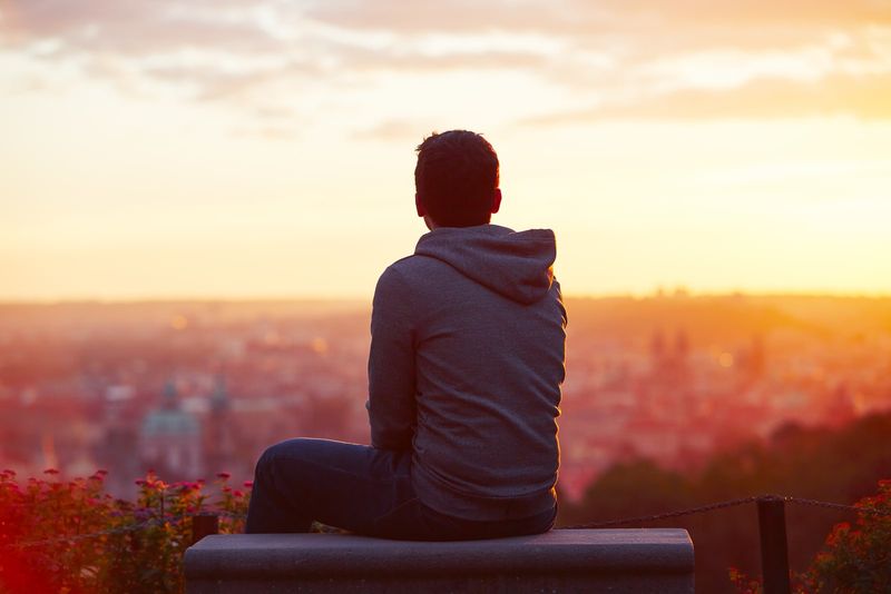 Ein junger Mann sitzt allein auf einem Felsen und beobachtet den Sonnenuntergang
