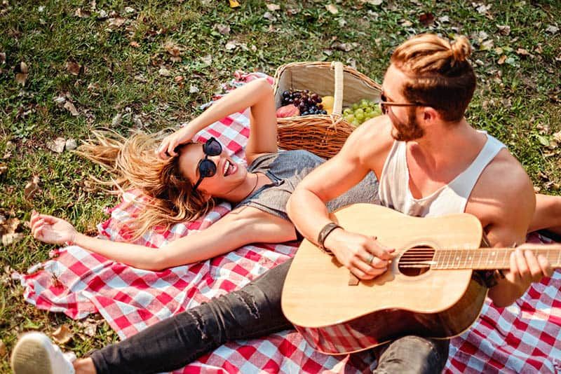 Mann, der während der Picknickzeit Gitarre zu lächelnder Frau spielt