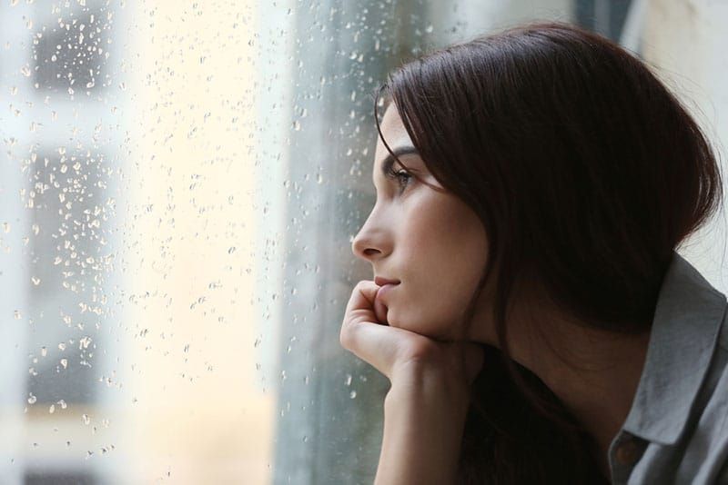 traurige Frau, die durch ein regnerisches Fenster schaut