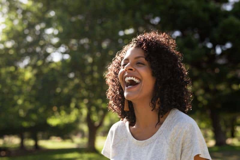 Lachende Frau mit lockigem Haar, während sie draußen in einem Park steht