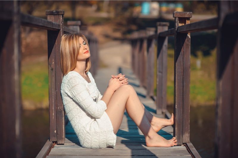 eine attraktive Blondine sitzt auf einer alten Holzbrücke