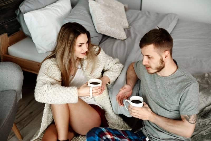 Junges Paar unterhält sich im Schlafzimmer mit Kaffee