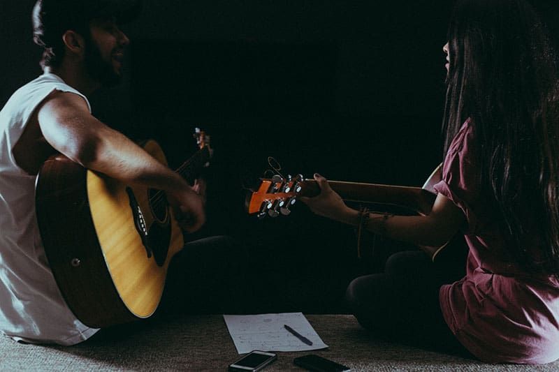 Mann und Frau spielen Gitarre an einem dunklen Ort